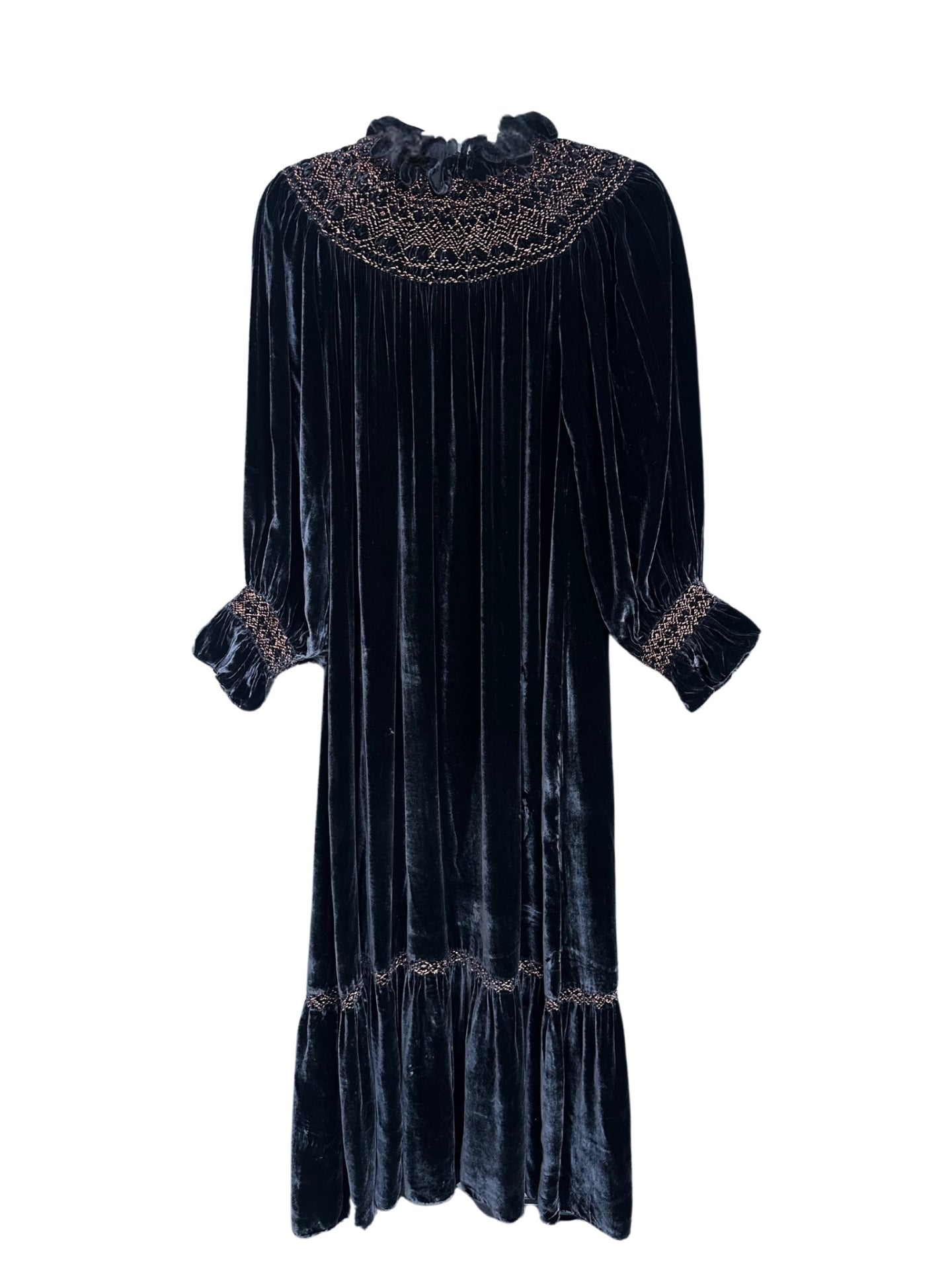 A front view of the Doen Viviana Velvet Dress, showcasing its deep navy color and luxurious texture. The dress features a high, ruffled neckline adorned with intricate beading and embroidery. Long sleeves gather at the wrists with elastic cuffs, and the dress falls gently to mid-calf with a ruffled hemline. The velvet fabric catches the light, creating a soft sheen throughout the dress.