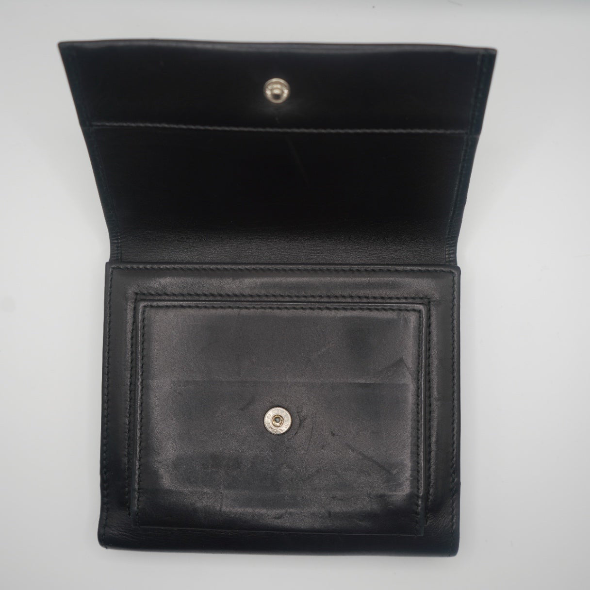An open view of the black leather Gucci bifold wallet, showing the interior. The left side features a secure compartment with a snap closure, while the smooth leather texture is visible throughout. The wallet's simple and elegant design highlights its practicality, offering a glimpse into its minimalist structure with a polished, luxurious finish.