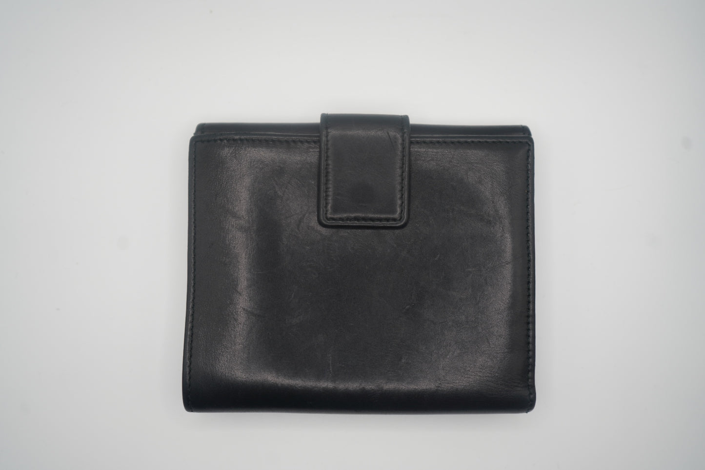 A front-facing view of a closed black leather Gucci bifold wallet, featuring a snap closure at the center. The smooth leather surface reflects light subtly, emphasizing the wallet's premium, minimalist design. The clean, elegant structure highlights its sophisticated craftsmanship.