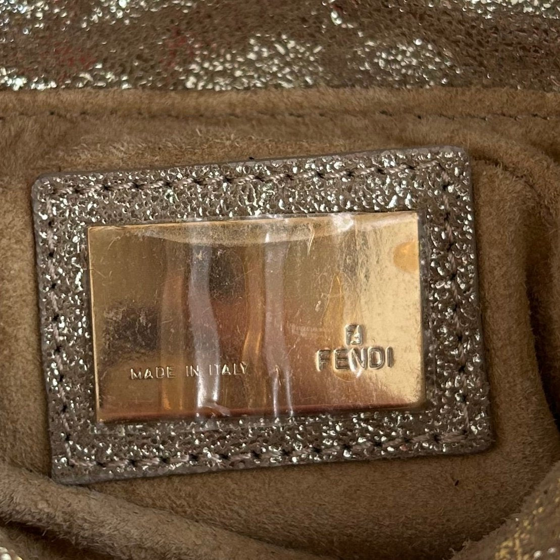 Close-up of the interior metal plaque of a 2004 Fendi Metallic Napa Mini Chef Shoulder Bag, engraved with 'Made in Italy' and the Fendi logo, highlighting its authenticity and luxury craftsmanship.