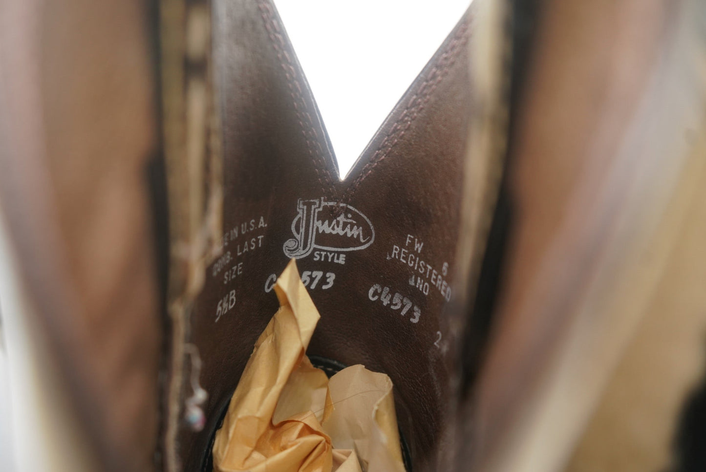 A close-up of the interior of a pair of Justin steel-toe fur cowboy boots, showing the stamped brand name and style details. The inside is lined with soft material, and the boot is partially stuffed with tissue paper. The style number and size are visible on the inside, offering a glimpse into the craftsmanship of the boots, designed for durability and comfort.