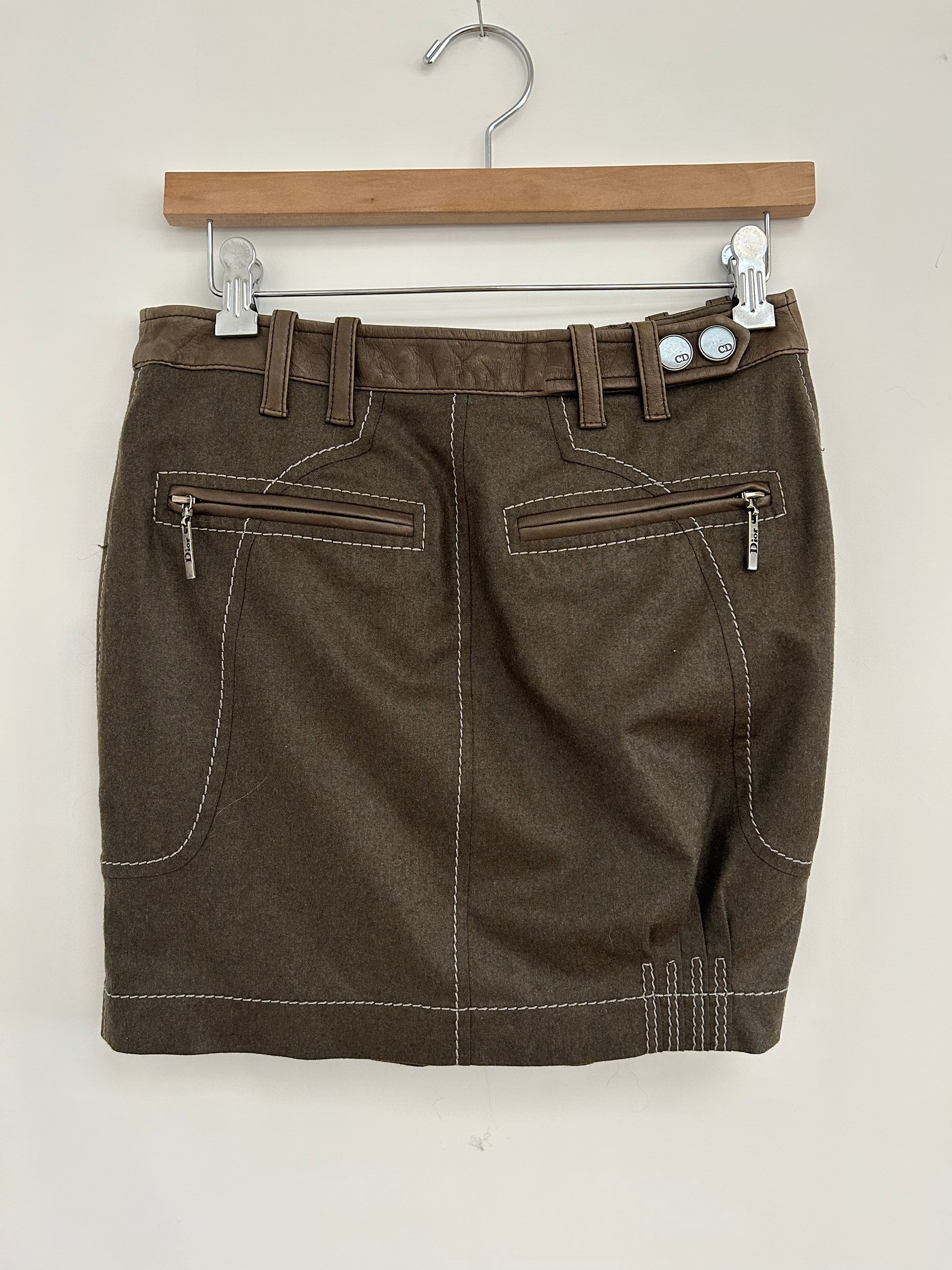Back view of a 2000s Christian Dior wool and lambskin mini skirt in brown, featuring zippered pockets, contrast stitching, and CD-branded button details. A sophisticated design showcasing Dior's signature craftsmanship and modern elegance.