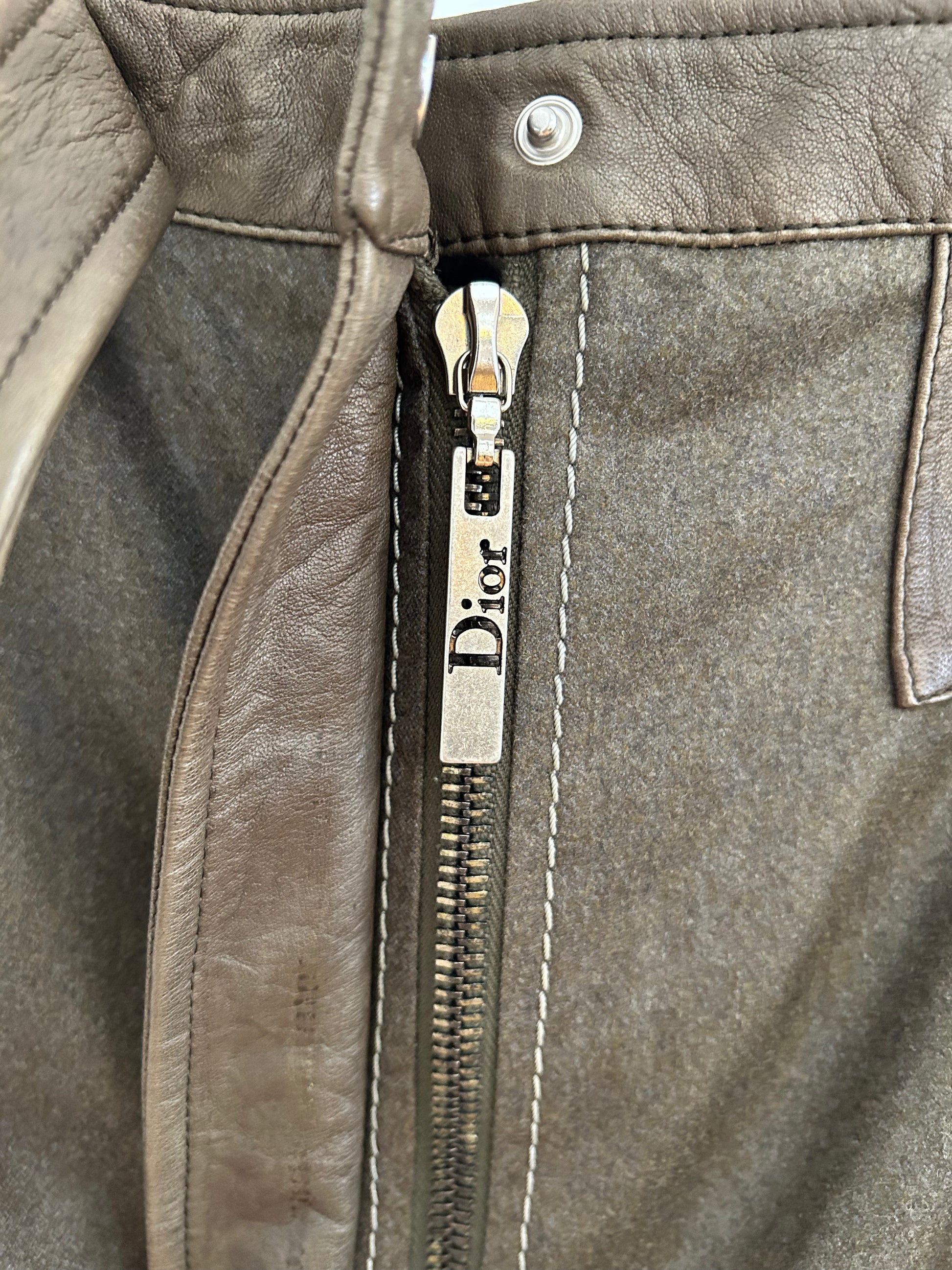 Detailed close-up of the Dior-branded zipper and leather trim on a 2000s Christian Dior wool and lambskin mini skirt, showcasing the premium materials, precise stitching, and elegant hardware of this luxury fashion piece.