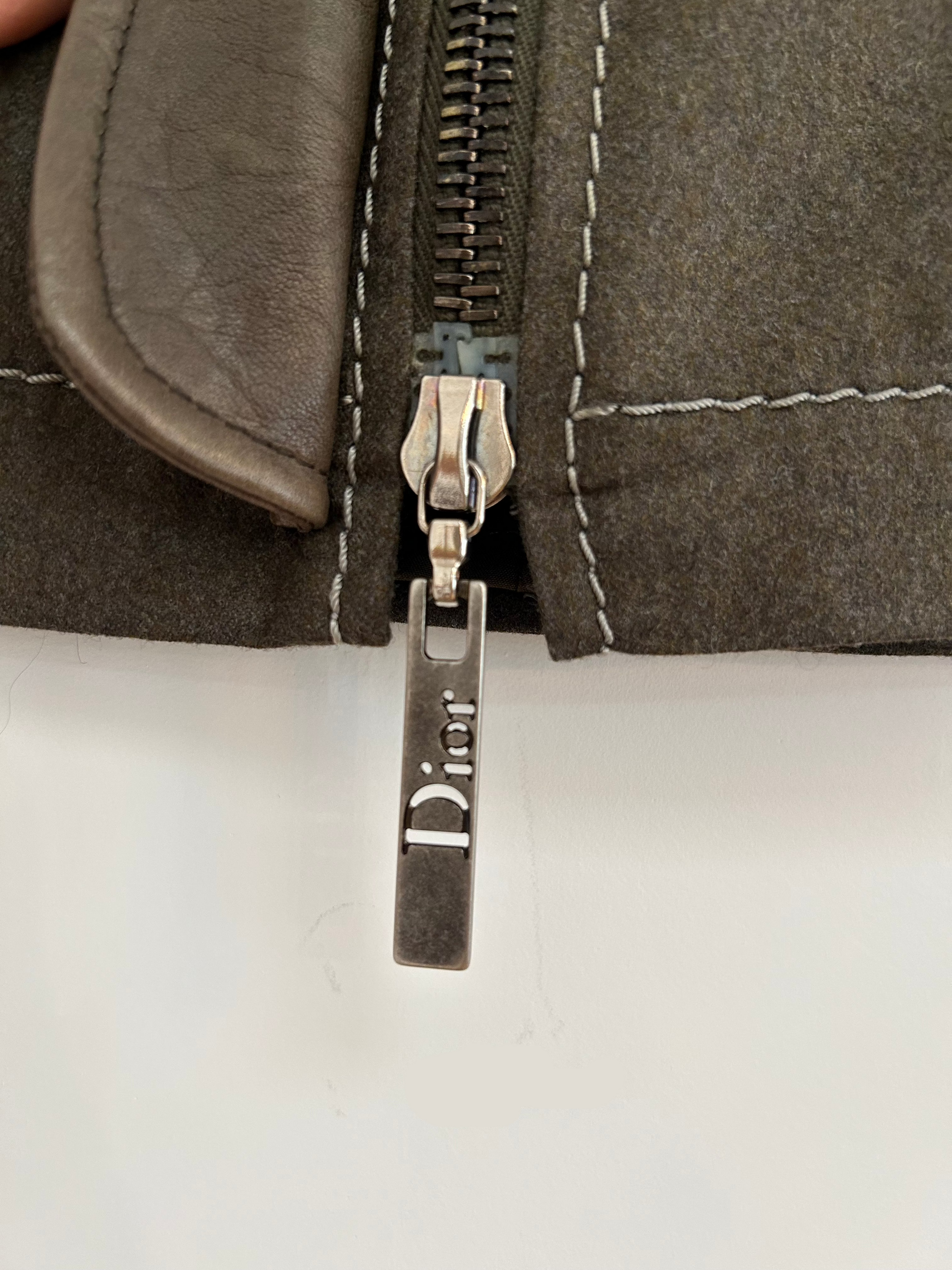 Close-up of the Dior-branded zipper pull on a 2000s Christian Dior wool and lambskin mini skirt, highlighting the intricate craftsmanship and luxurious details of this iconic piece.