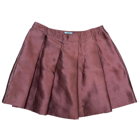 Front view of a Miu Miu mini skirt in a metallic burgundy fabric with a structured silhouette. The skirt features sharp pleats for added volume and a clean waistband design.